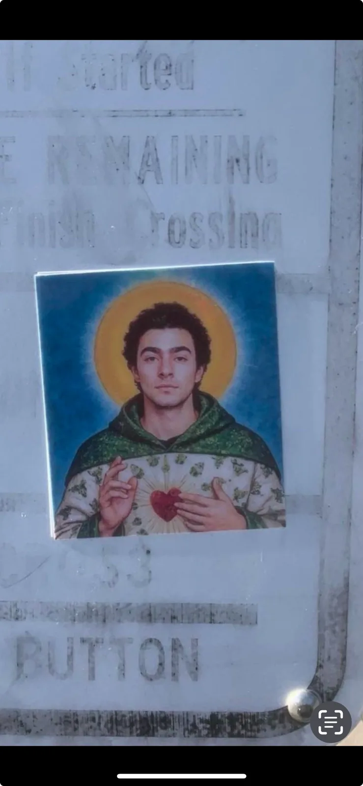 A sticker of a man with a halo and a glowing heart on his chest is taped over a worn metal panel. The panel has faded…