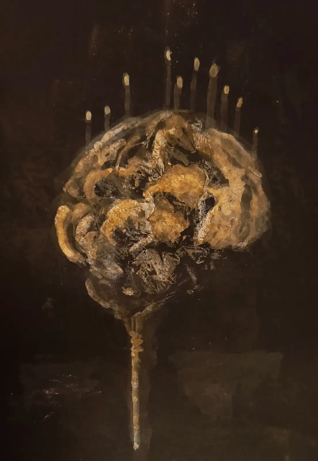 A close-up image shows a dark, textured, brain-like object with a crown of lit candles on top, set against a black…