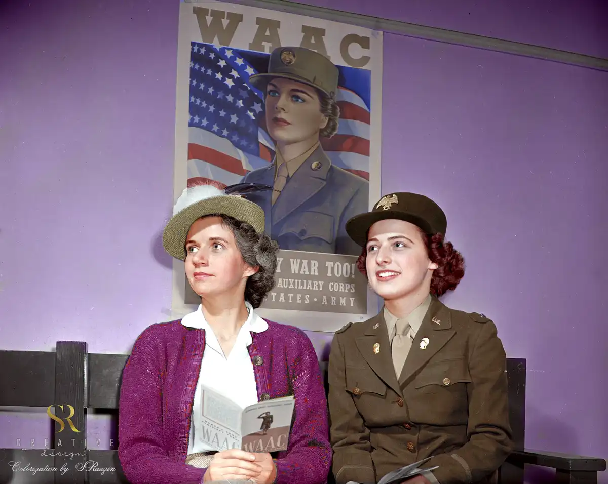 Two women sit on a bench in front of a vintage WAAC (Women's Army Auxiliary Corps) recruitment poster featuring a woman in…