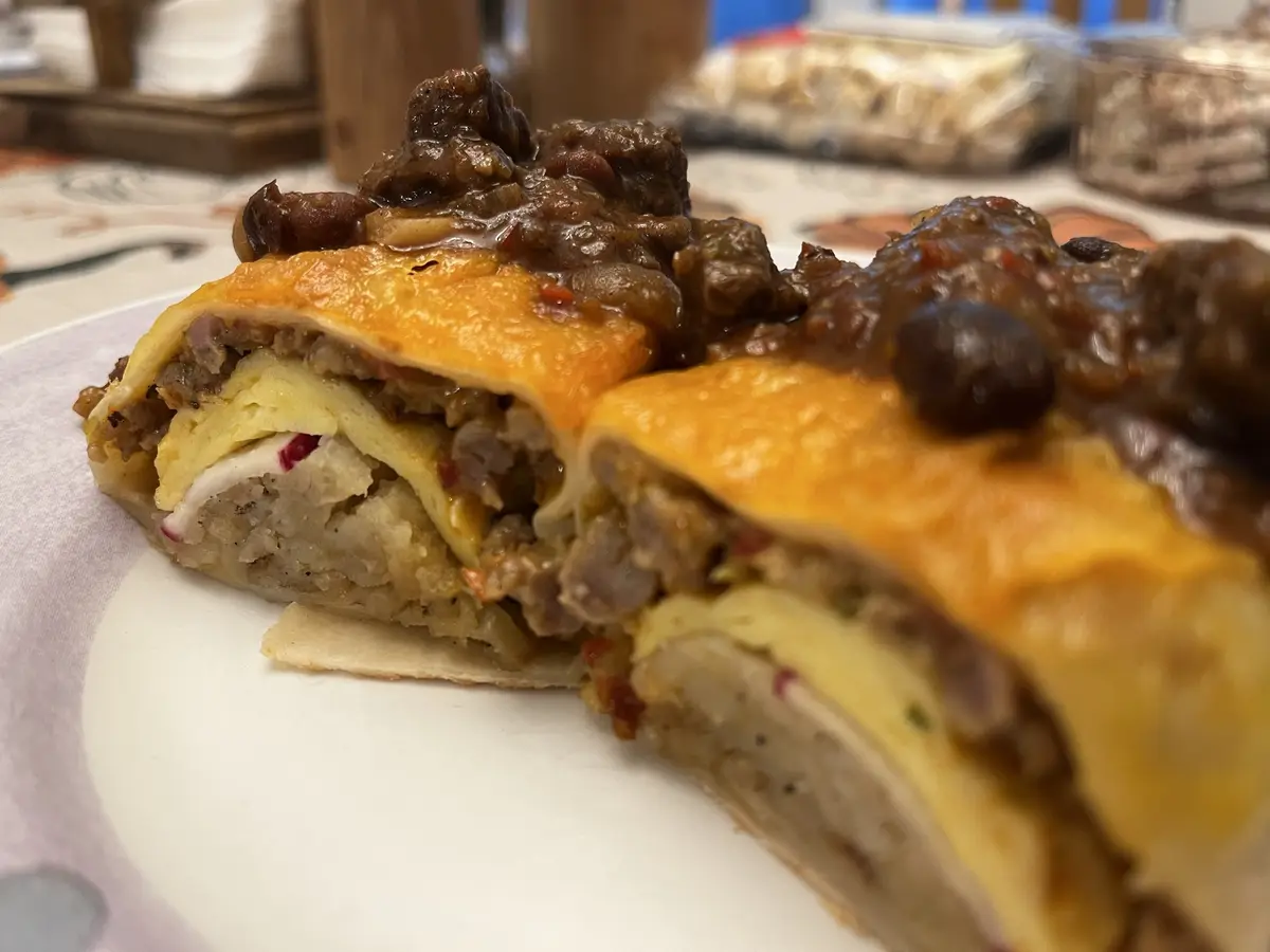 A close-up photo shows two halves of a rolled, cheesy, meat-filled dish on a white plate, topped with a dark, chunky sauce…