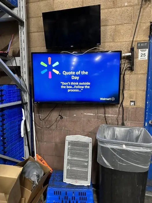 A blue Walmart TV screen mounted on a brick wall displays the 'Quote of the Day' as 'Don't think outside the box...Follow…