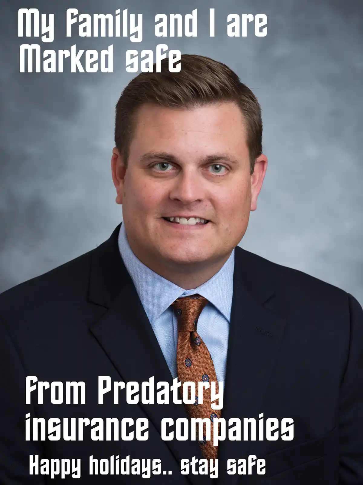 A professional headshot of a smiling man in a dark suit, light blue shirt, and patterned tie against a gray studio…