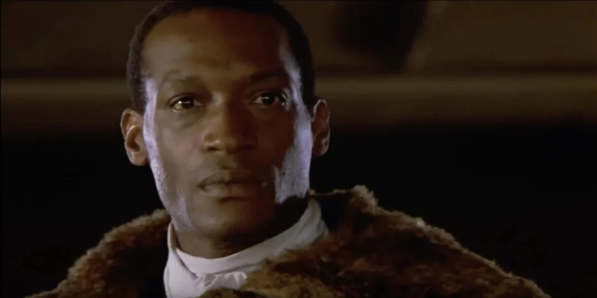 A close-up of a man with a serious, unimpressed expression, wearing a brown fur collar over a white shirt and bowtie. The…