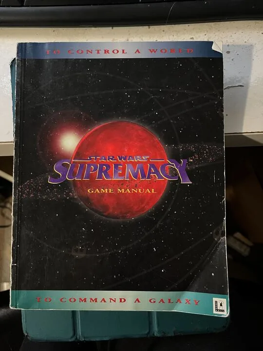 A worn, physical copy of the 'Star Wars Supremacy Game Manual' is shown, featuring a red planet against a starry background…