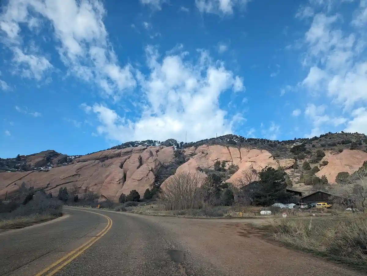 A scenic photo of a winding road curving through a desert landscape with large red rock formations under a bright blue sky…