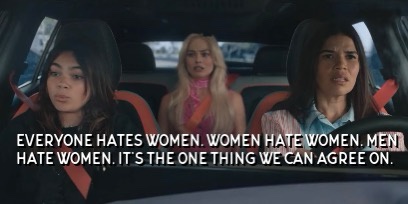 Three women are seated in a car, looking concerned or annoyed. The woman in the driver's seat has dark hair and a serious…