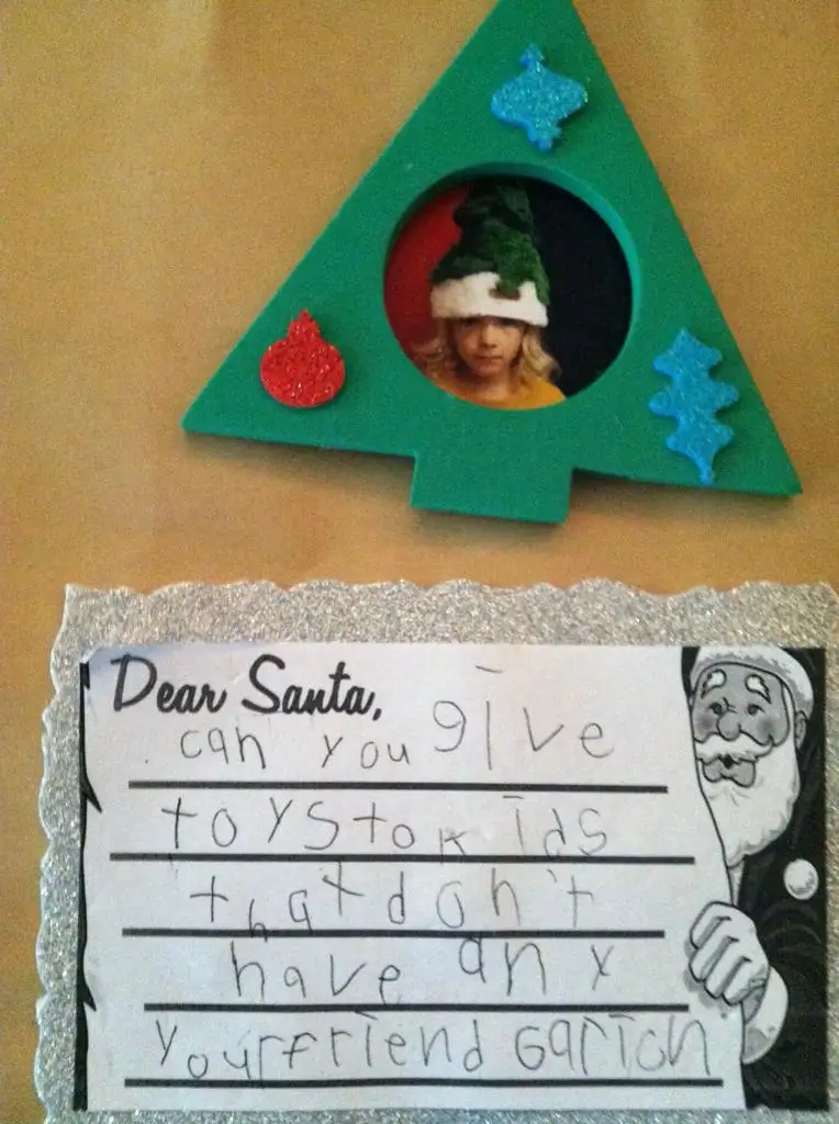 A child's handwritten Christmas letter to Santa is displayed below a green paper Christmas tree decoration with a circular…