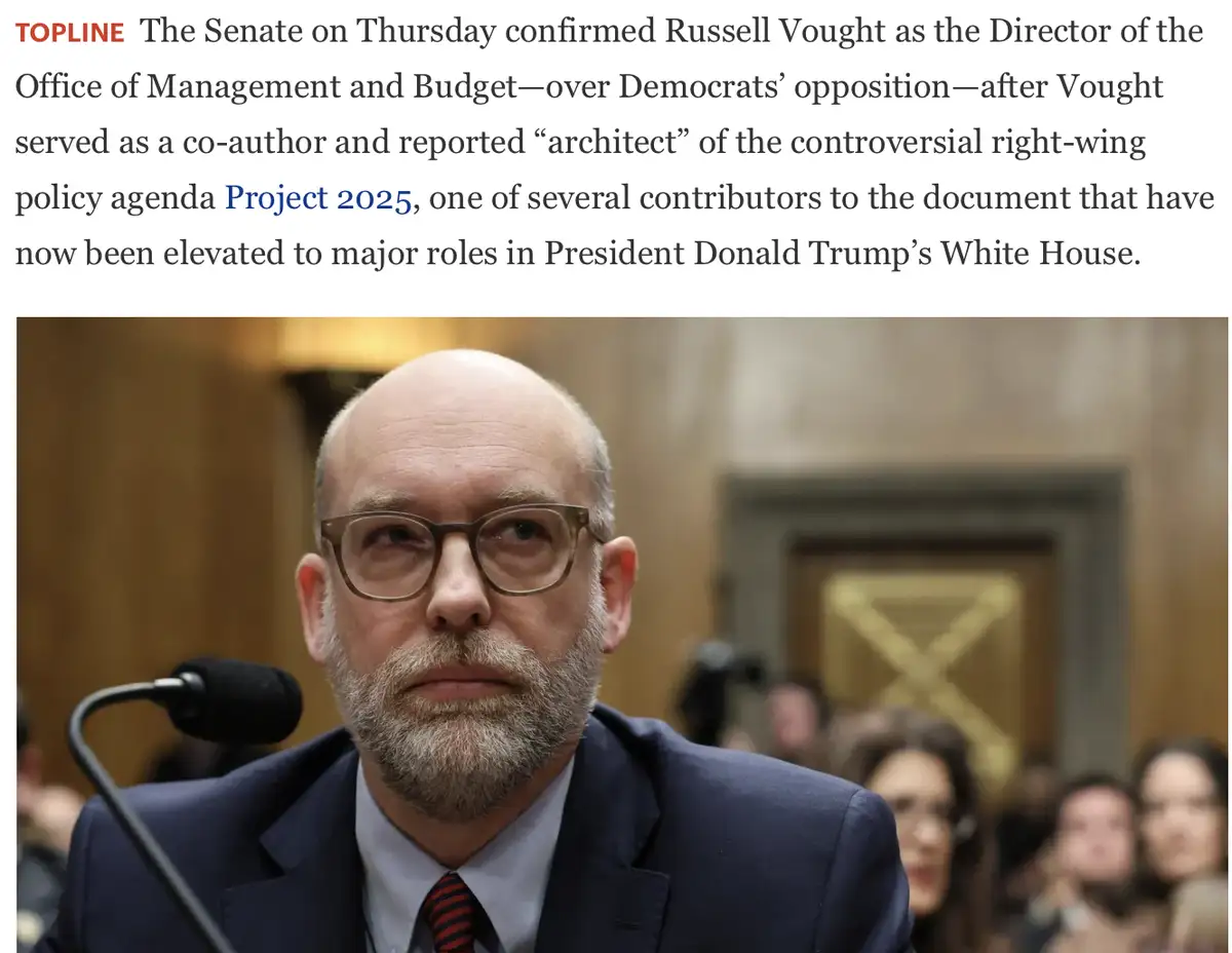 A photo of Russell Vought, a bald man with glasses and a beard wearing a suit and tie, seated at a hearing with a…