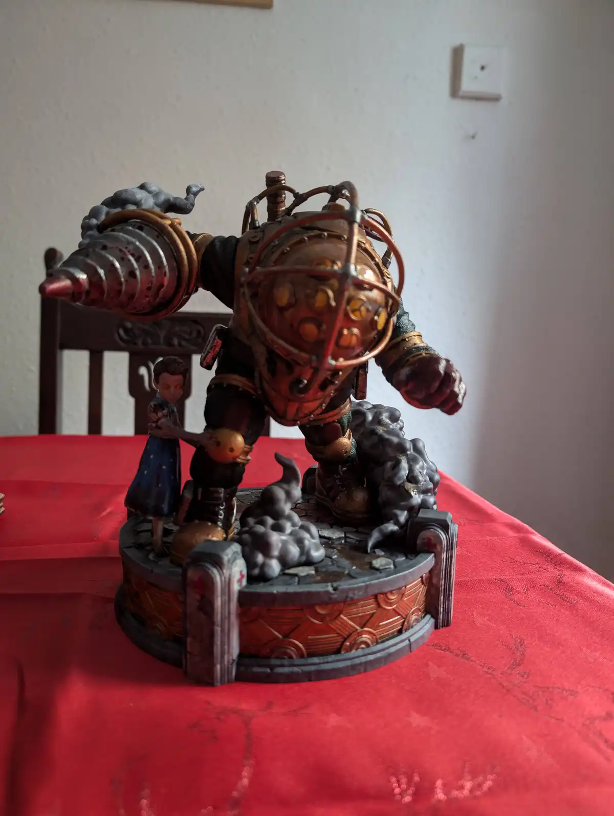 A figurine of a large, armored, steampunk-style robot with a drill arm and glowing eyes stands on a circular base with a…