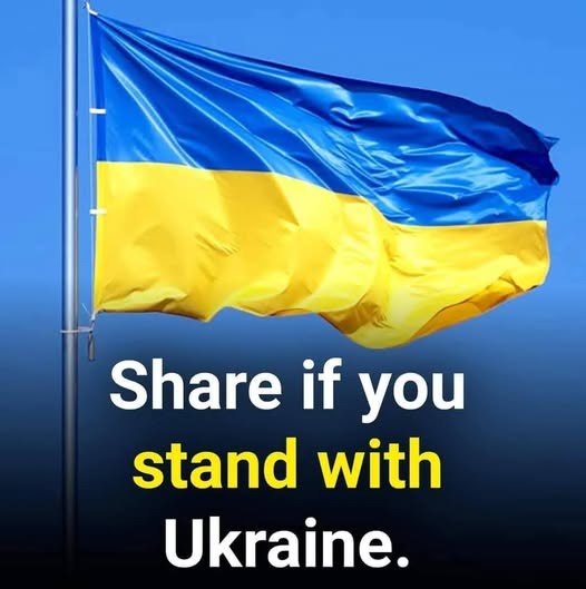 A Ukrainian flag, with its blue and yellow horizontal stripes, is shown waving in the wind against a clear blue sky. White…