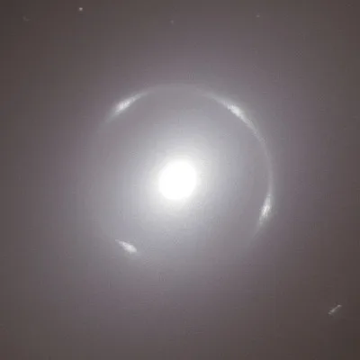 A blurry, low-resolution image shows a bright, glowing orb with a faint halo or ring around it, set against a dark…