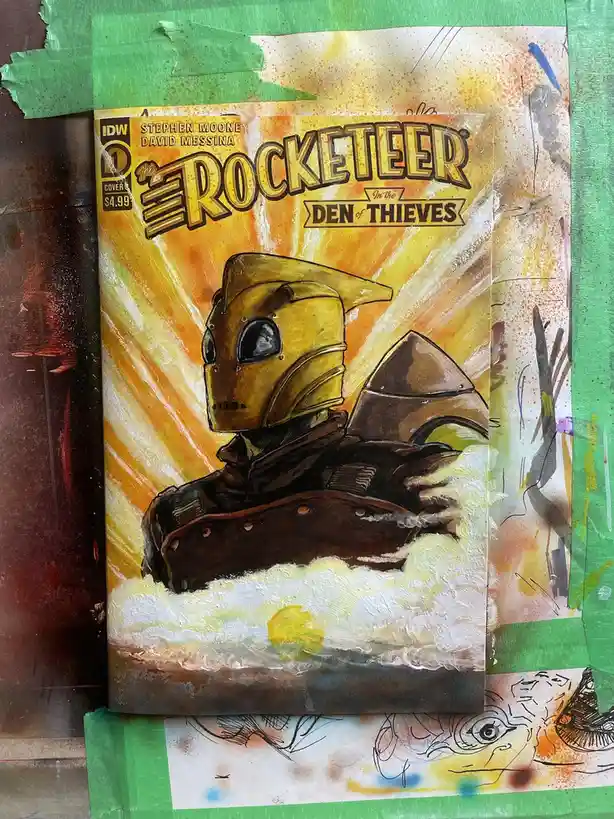 A comic book cover of 'The Rocketeer: In the Den of Thieves' by IDW, featuring the titular character in his iconic gold…