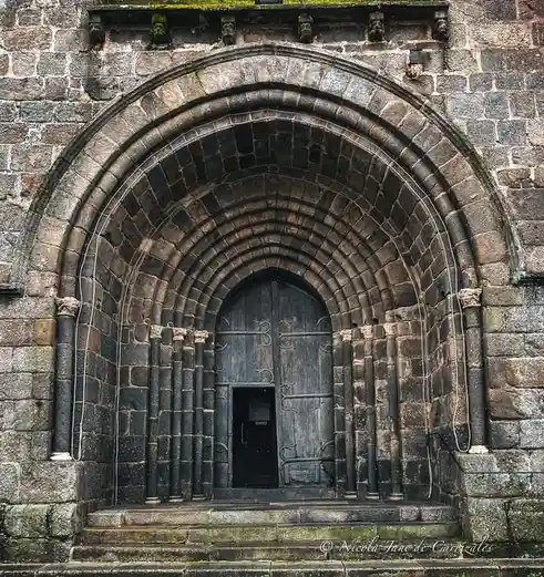 A close-up photo of an old stone church entrance with a large arched doorway and heavy wooden doors. Two thin white wires…