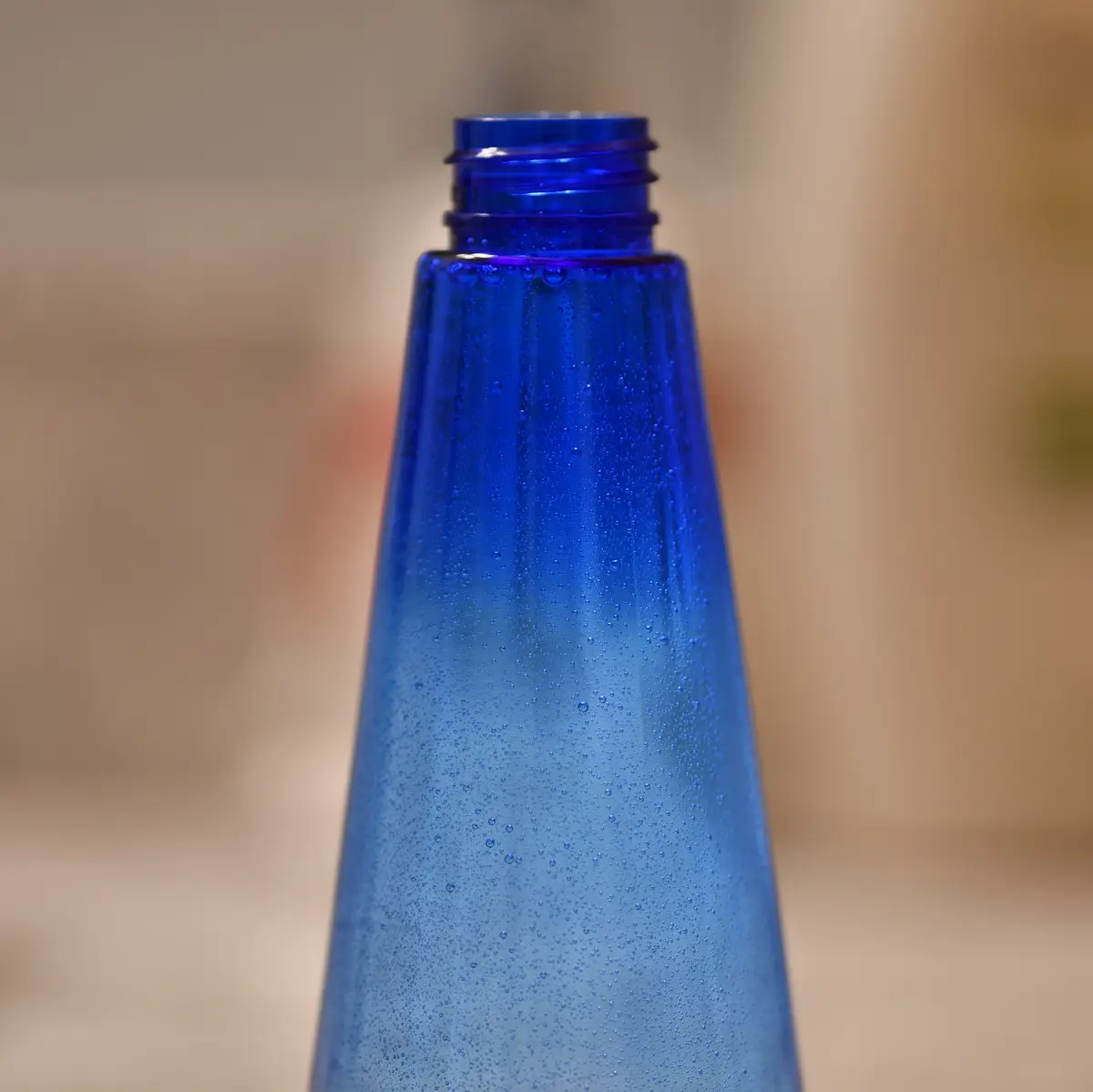 A close-up photo shows the top of a blue plastic bottle, its surface covered in tiny water droplets or bubbles, with a…
