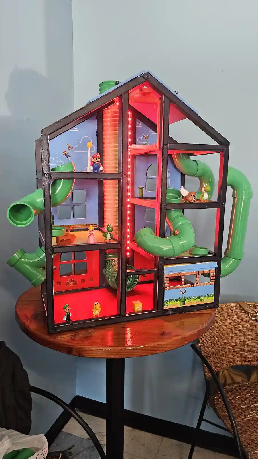 A custom-built, multi-level dollhouse constructed with a black metal frame and decorated with Mario-themed elements…
