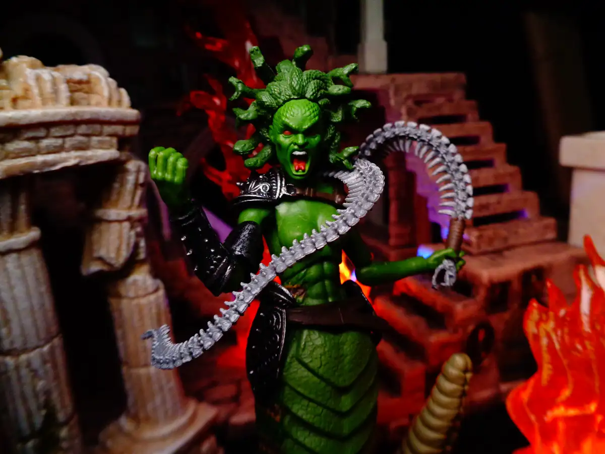 A green, reptilian demon figurine with a snake-like head and a curved, serrated sword stands in a fiery, ruinous setting…
