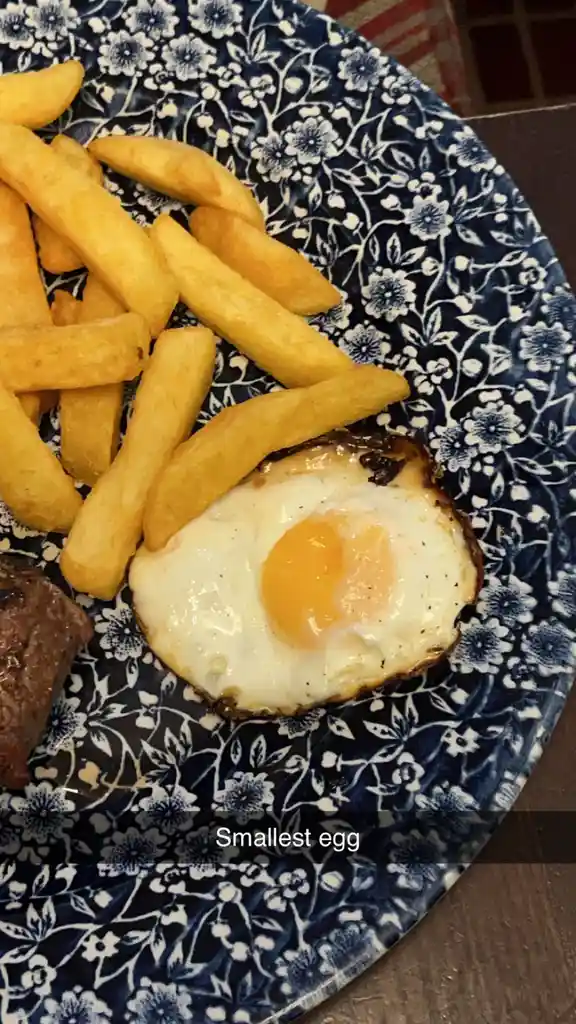 A close-up photo of a meal on a blue and white floral plate, featuring a single fried egg, golden french fries, and a piece…
