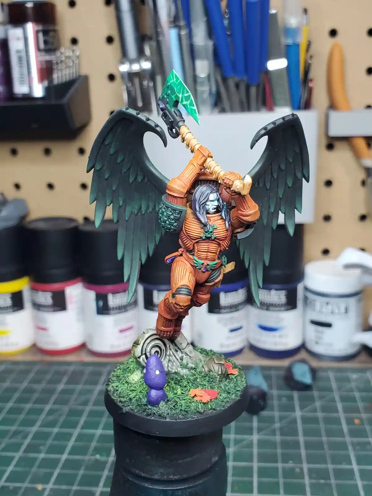 A highly detailed, painted fantasy miniature of a winged warrior in orange armor, wielding a large axe with a green blade…