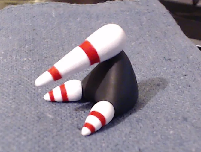 A handmade figurine of a bowling pin with a black, cone-shaped body and three white-and-red striped legs, posed as if…