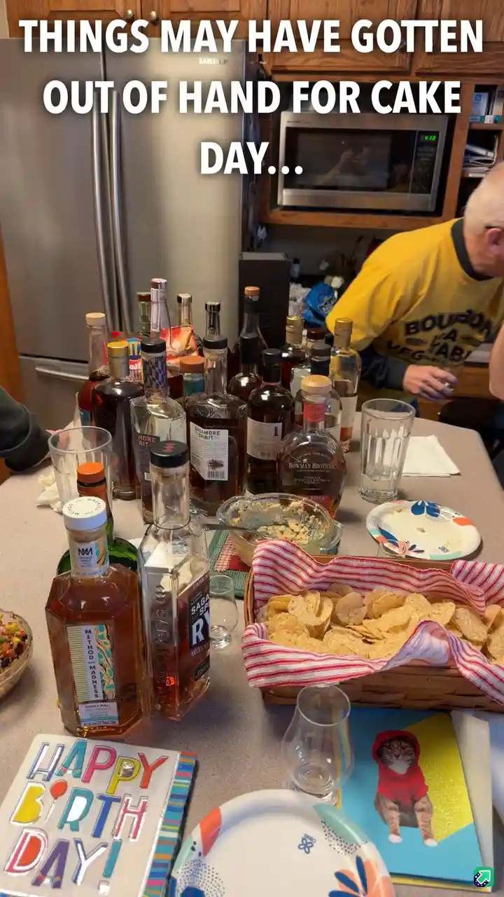 A kitchen counter is cluttered with numerous liquor bottles, empty glasses, a basket of tortilla chips, and a 'HAPPY…