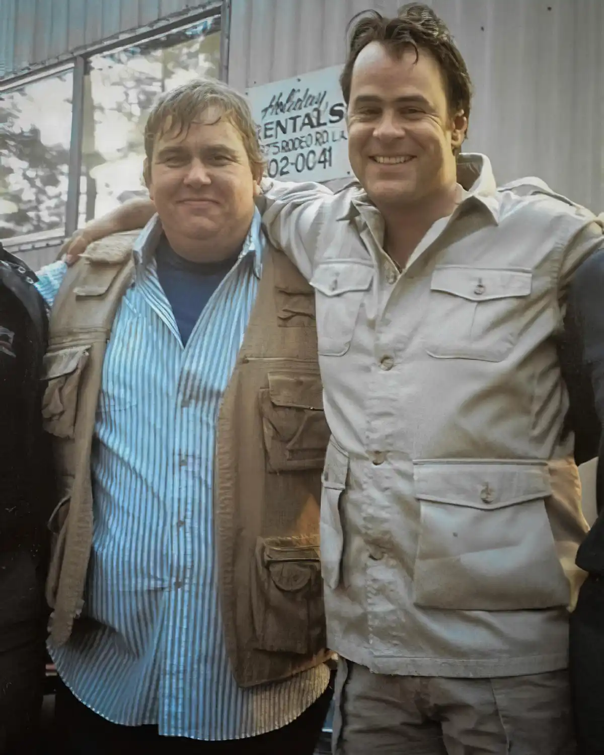 Two men stand side by side, one with his arm around the other. The man on the left has a smug, unimpressed expression while…