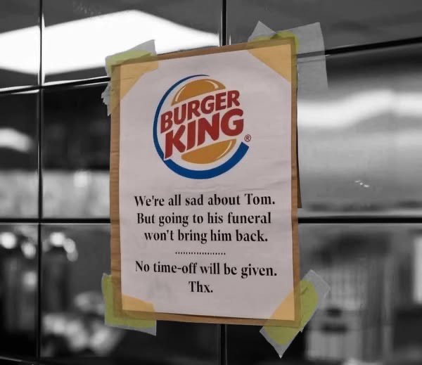 A Burger King sign taped to a glass door, with black-and-white background. The sign features the Burger King logo and text…