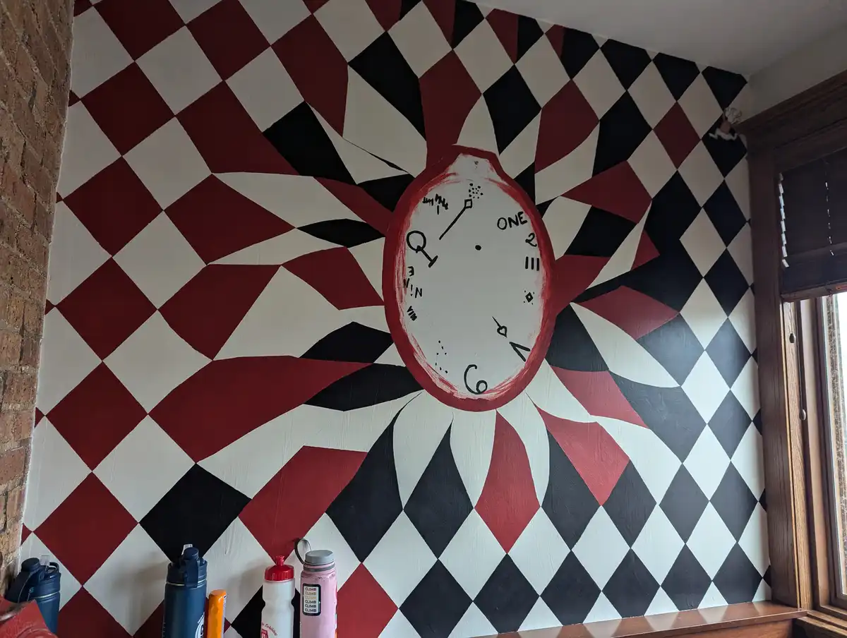 A wall painted with a red, black, and white harlequin pattern features a large, hand-painted clock face with numbers like…