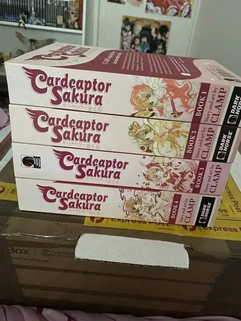 Four boxes of the 'Cardcaptor Sakura' manga series, labeled Book 1 through Book 4, are stacked vertically on top of a…