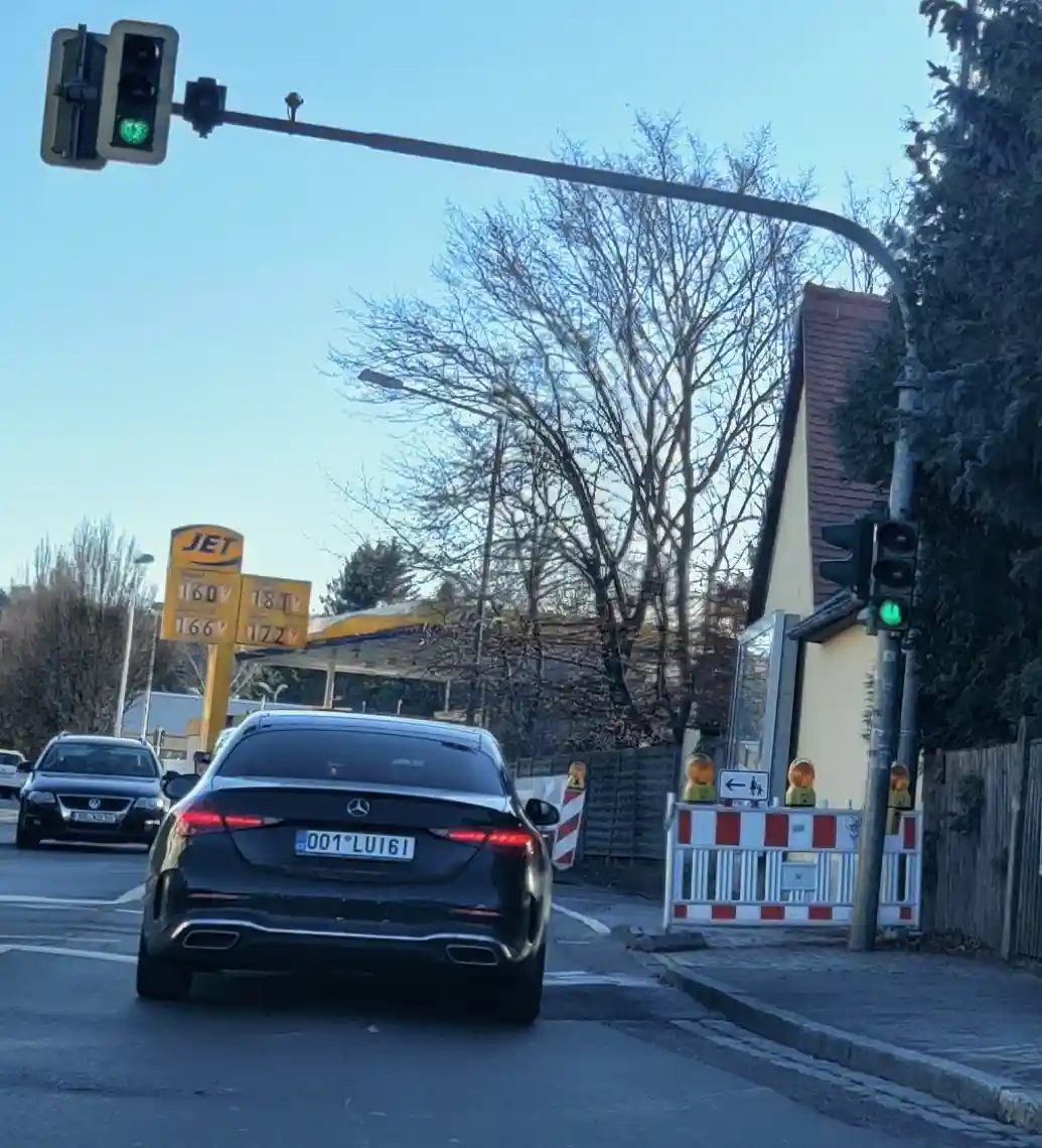 A black Mercedes-Benz sedan is stopped at a green traffic light on a street with a JET gas station sign visible in the…