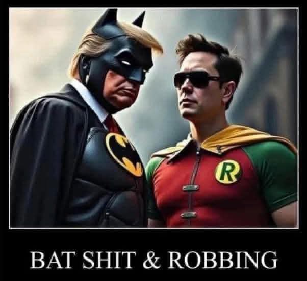Two men in superhero costumes stand side by side; the one on the left wears a Batman cowl with a blonde wig resembling…