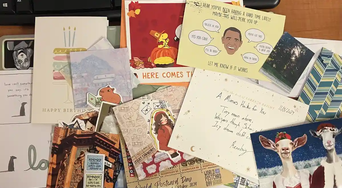 A pile of assorted greeting cards and postcards on a desk, including a prominent yellow card featuring a cartoon caricature…