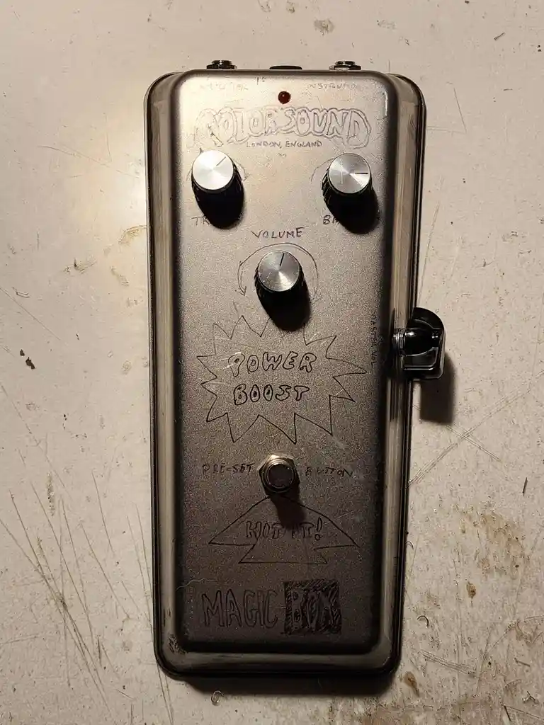 A close-up of a worn, silver guitar effects pedal with handwritten text. The pedal has three knobs labeled 'TR', 'VOLUME'…