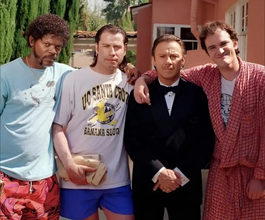 Four men pose together outdoors; from left to right, one wears a light blue t-shirt and patterned shorts, another wears a…