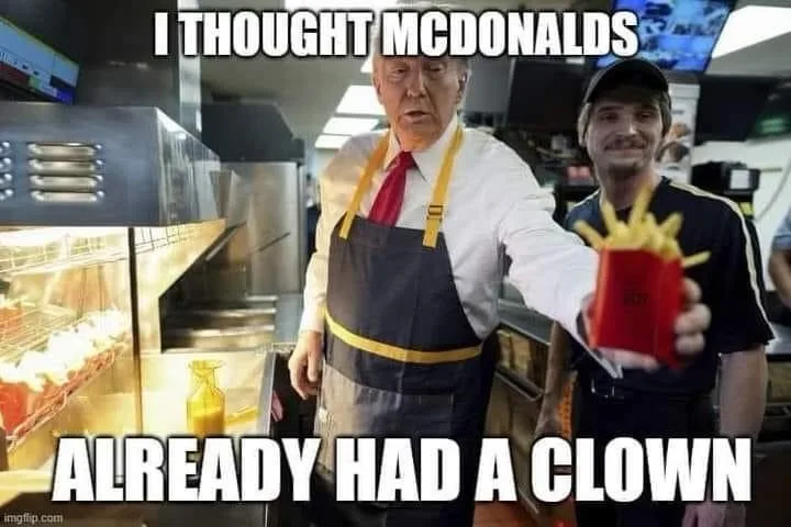 A man in a McDonald's uniform with a red tie and yellow apron holds up a red fry container, looking surprised. Behind him…