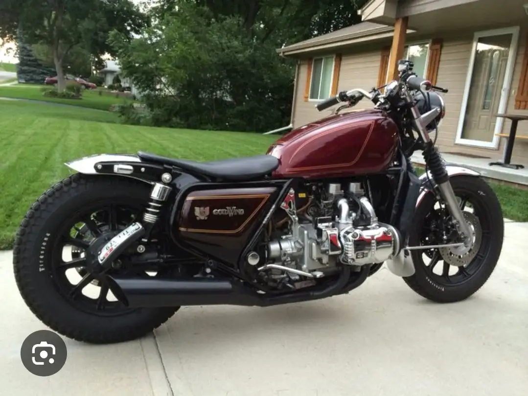 A custom-built motorcycle with a maroon fuel tank, black frame, and chrome engine sits parked on a concrete driveway in…
