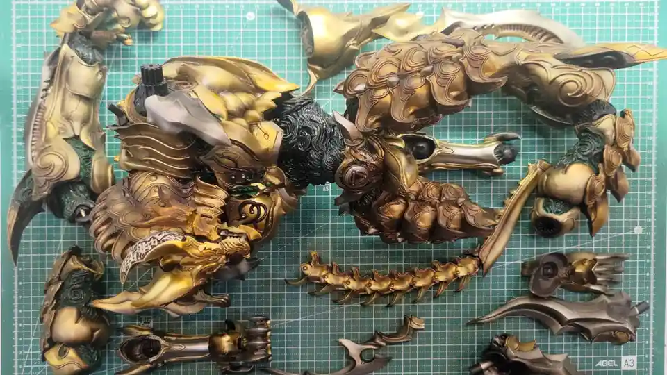 A highly detailed, gold and black painted model kit of a fantasy creature, possibly a dragon or chimera, is shown…