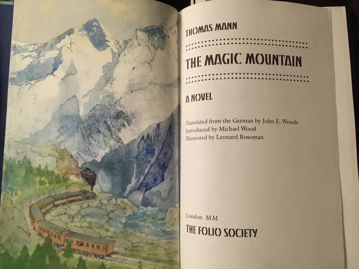 An open book displays the title page of Thomas Mann's 'The Magic Mountain,' featuring a watercolor illustration of a train…