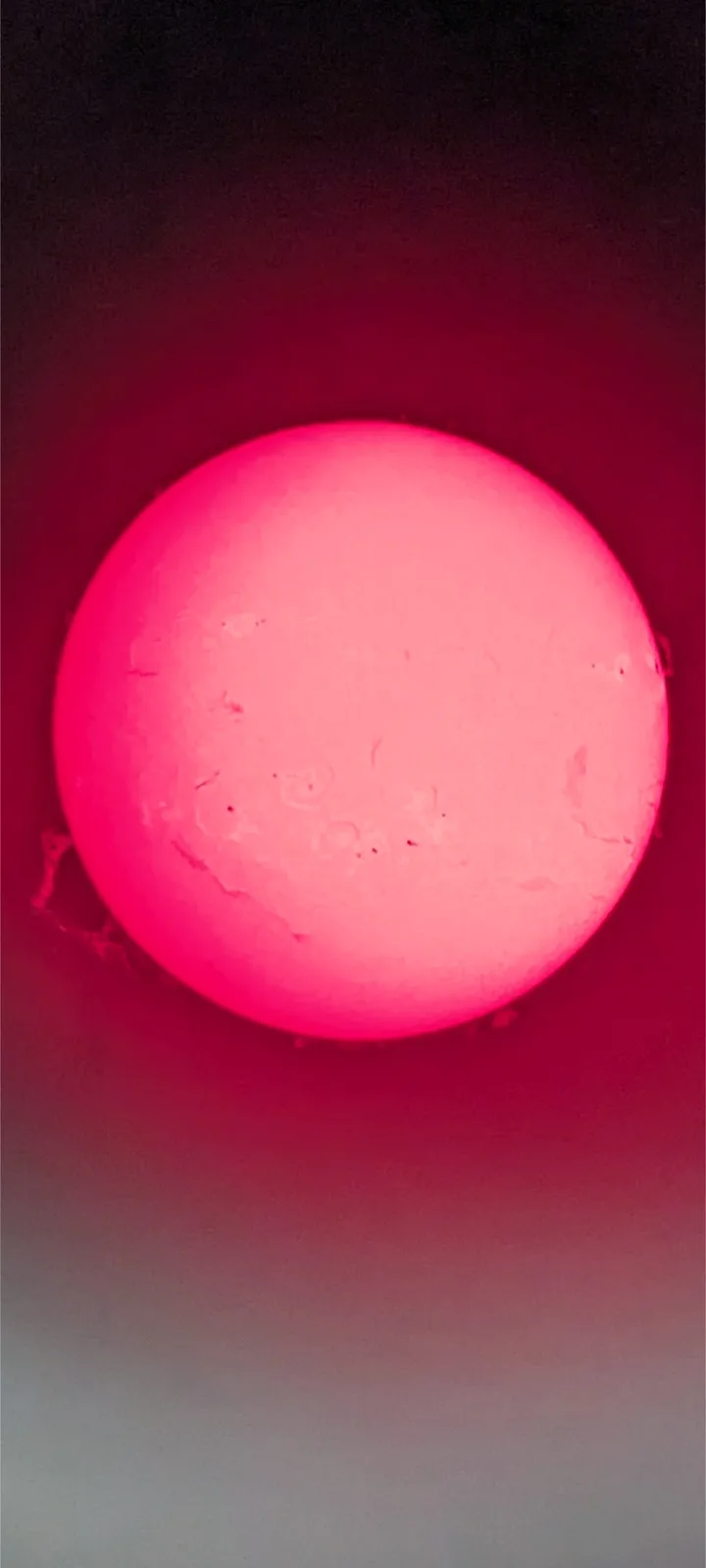 A close-up photo shows a large, glowing pinkish-red circular object, resembling the sun, with visible surface texture and…