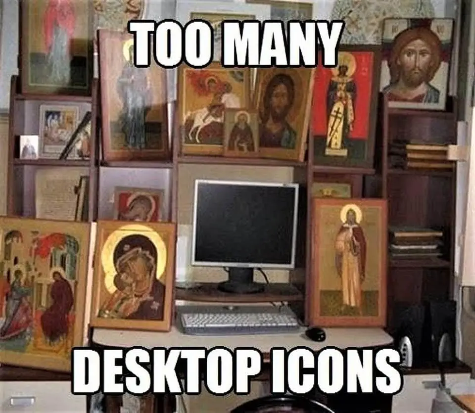 A computer monitor sits on a desk surrounded by numerous framed religious icons, filling shelves and surfaces around it. The…