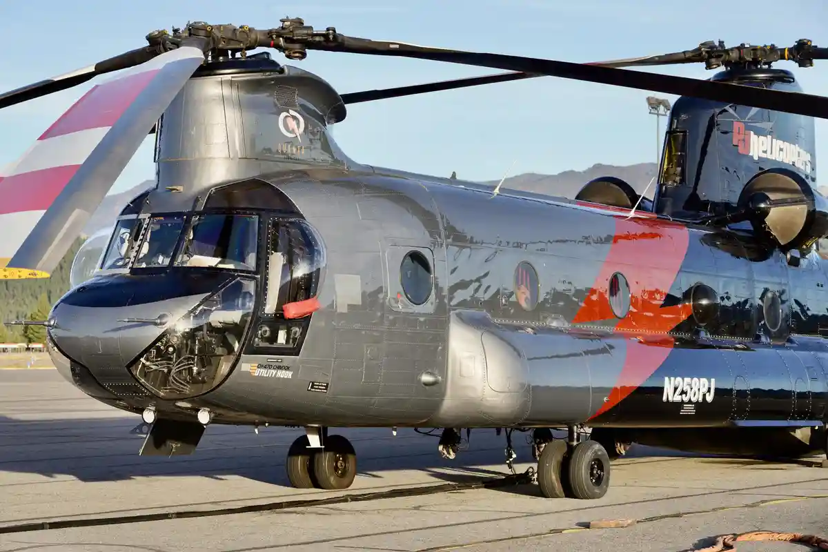 A large, gray and red CH-47D Chinook helicopter with 'QUANTA SERVICES' and 'N258PJ' markings is parked on an airfield. The…