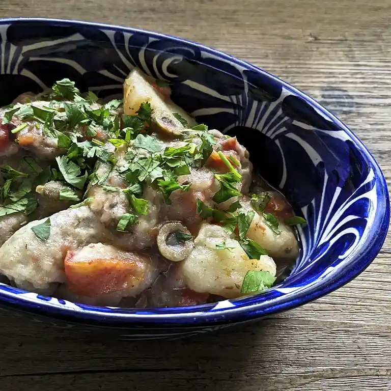 A close-up photo shows a blue and white patterned ceramic bowl filled with a hearty stew containing chunks of meat…