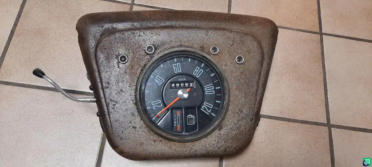 A rusty, vintage motorcycle speedometer with a mechanical odometer reading 49052 km/h is shown resting on a tiled floor. The…