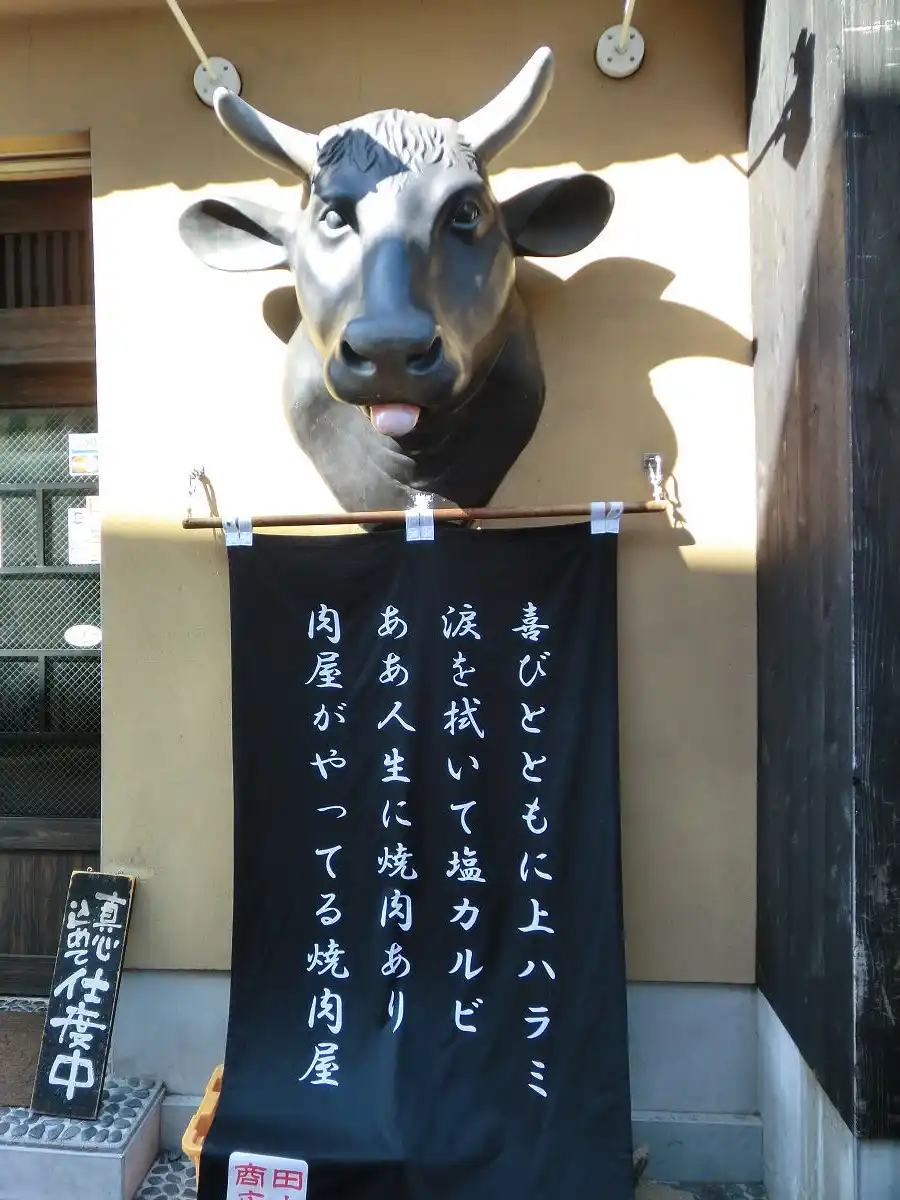 A large, realistic statue of a cow's head with its tongue sticking out is mounted on a building wall, above a black banner…