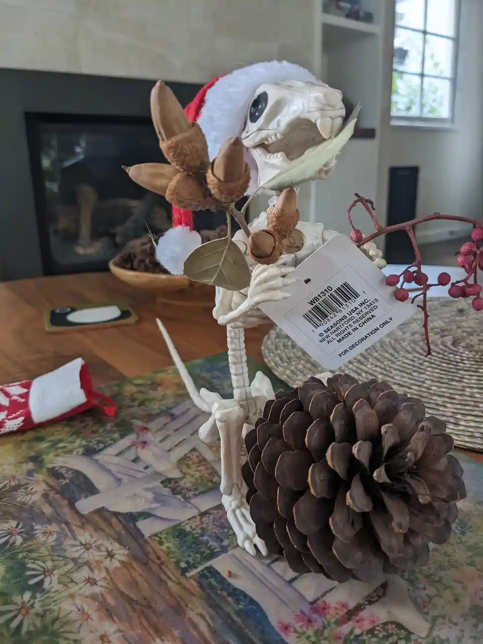 A plastic skeleton of a rodent, wearing a red and white Santa hat, is posed holding acorns and leaves while standing next to…