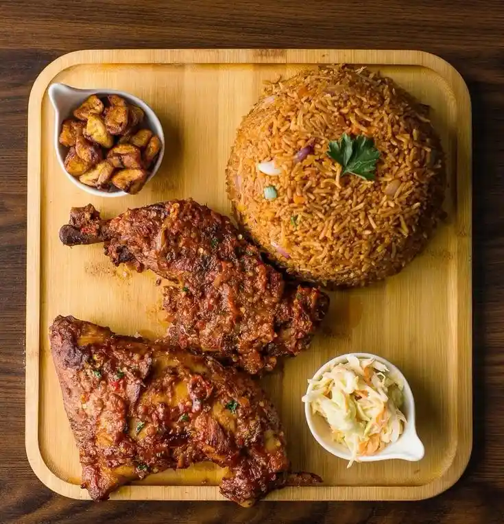 a top-down photo of a wooden tray holding a large dome of seasoned rice, two pieces of meat covered in red sauce, a small…