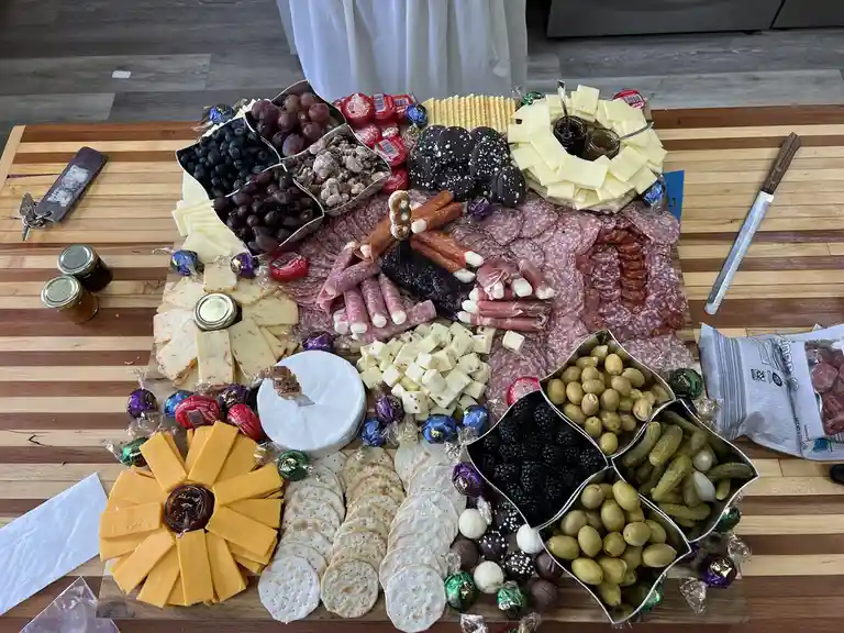 An overhead photo of an elaborate charcuterie board on a wooden cutting board, filled with various cheeses, meats, olives…