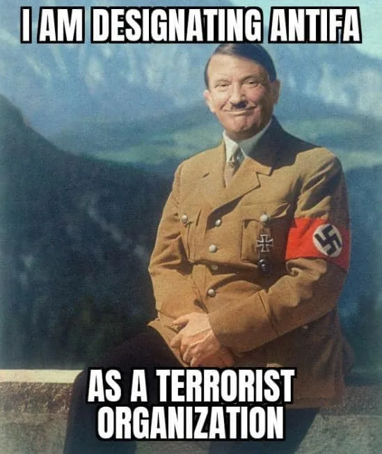 A historical photograph of Adolf Hitler in a brown Nazi uniform with a swastika armband, smiling while seated outdoors with…