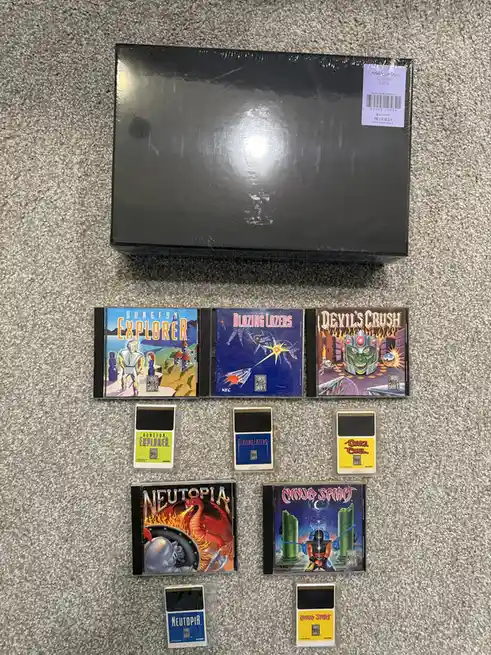 A black, sealed box labeled 'Analogue Duo Console [JPN]' sits atop a grey carpet, surrounded by five TurboGrafx-16 game…