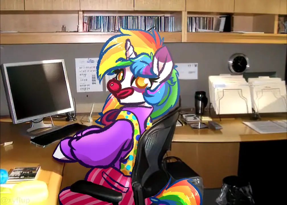 A cartoon pony with rainbow hair and a clown nose is sitting in an office chair at a desk with a computer monitor, keyboard…