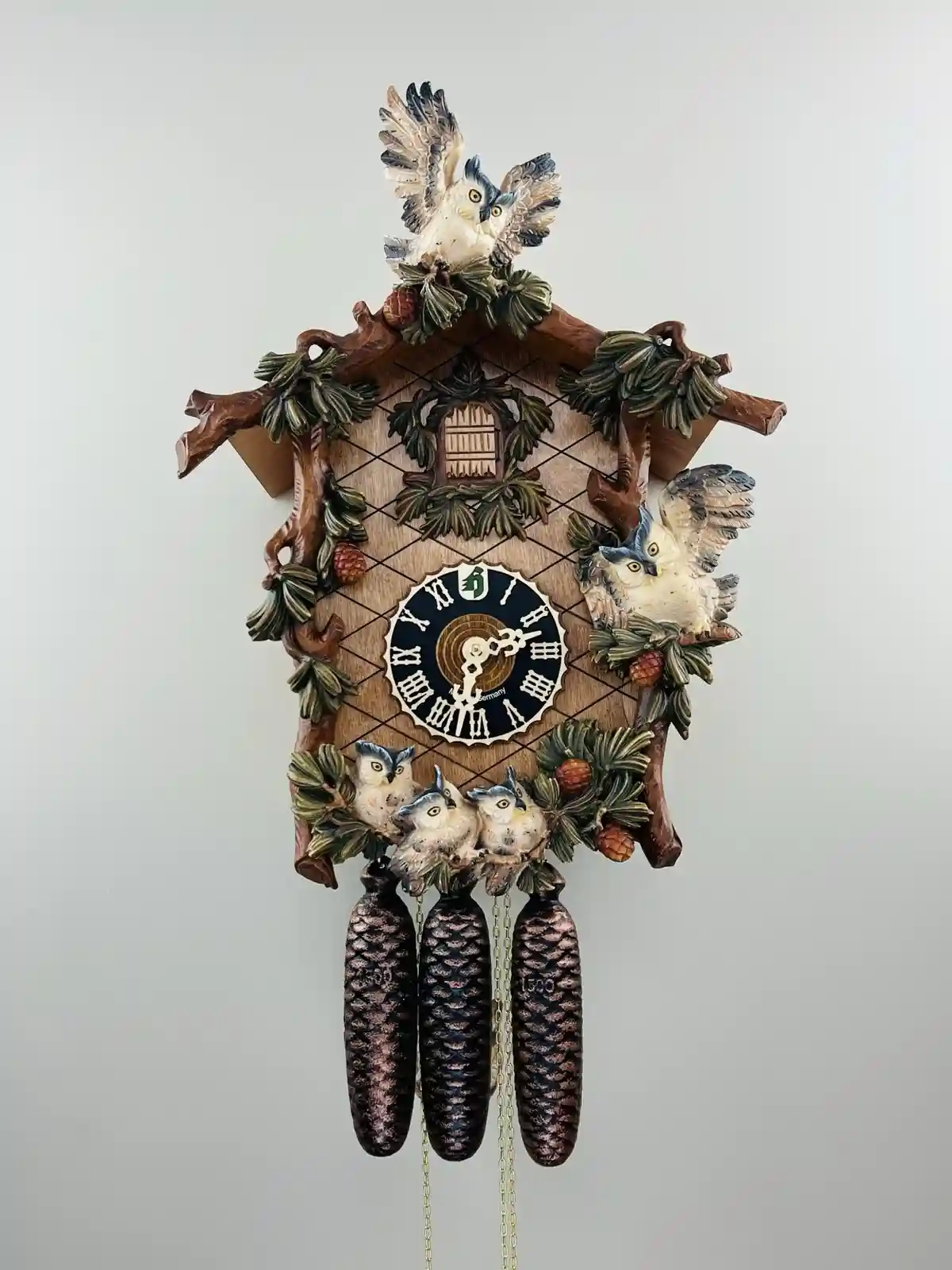 A decorative cuckoo clock with carved wooden owl figures, pinecone weights, and Roman numerals, overlaid with the text 'I'm…